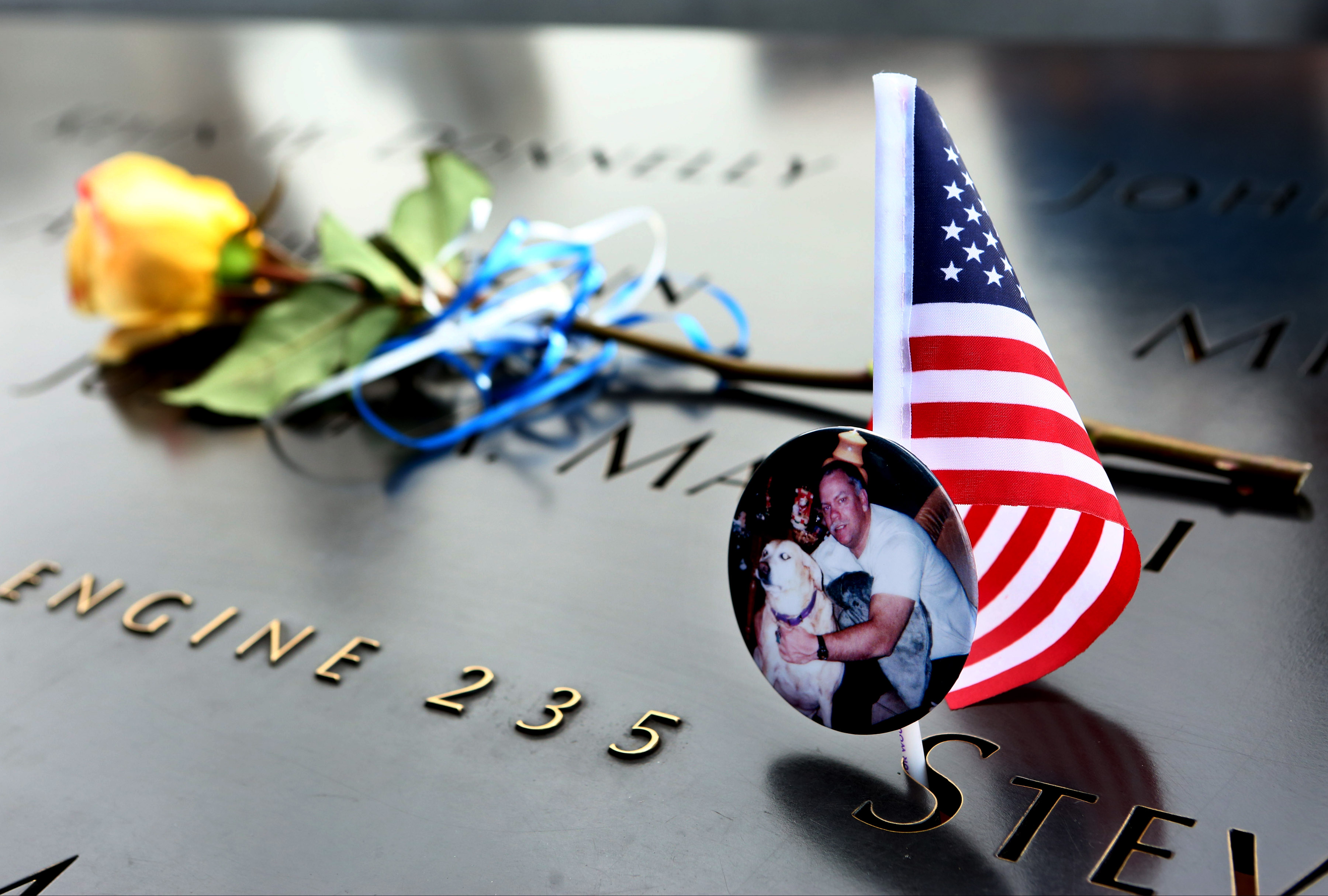 A small American flag, a yellow rose, and a photo of a victim have been left at a name on the 9/11 Memorial.