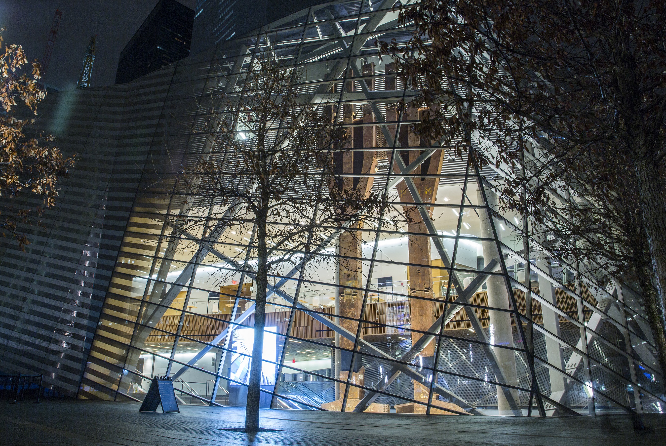 The interior of the Museum pavilion can be seen illuminated at night from outside on Memorial plaza. The steel tridents from the Twin Towers can be seen through the glass of the pavilion.