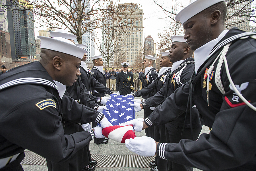 Formally-dressed members of the United States Navy Ceremonial Guard fold an American flag during a ceremony at the 9/11 Memorial.