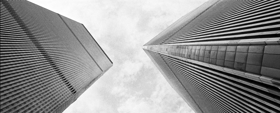 This old, black-and-white photo of the World Trade Center shows the Twin Towers from below on the plaza.