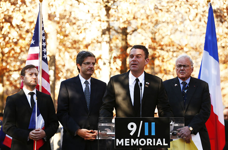 9/11 Memorial President Joe Daniels speaks to a crowd on the Memorial plaza during a tribute for the victims of the Paris, France, terrorist attacks. He is flanked by Consul General of France in New York Bertrand Lortholary, representative of France to the United Nations Francois Delattre and 9/11 Memorial board member and former U.S. ambassador to France Joe Daniels.