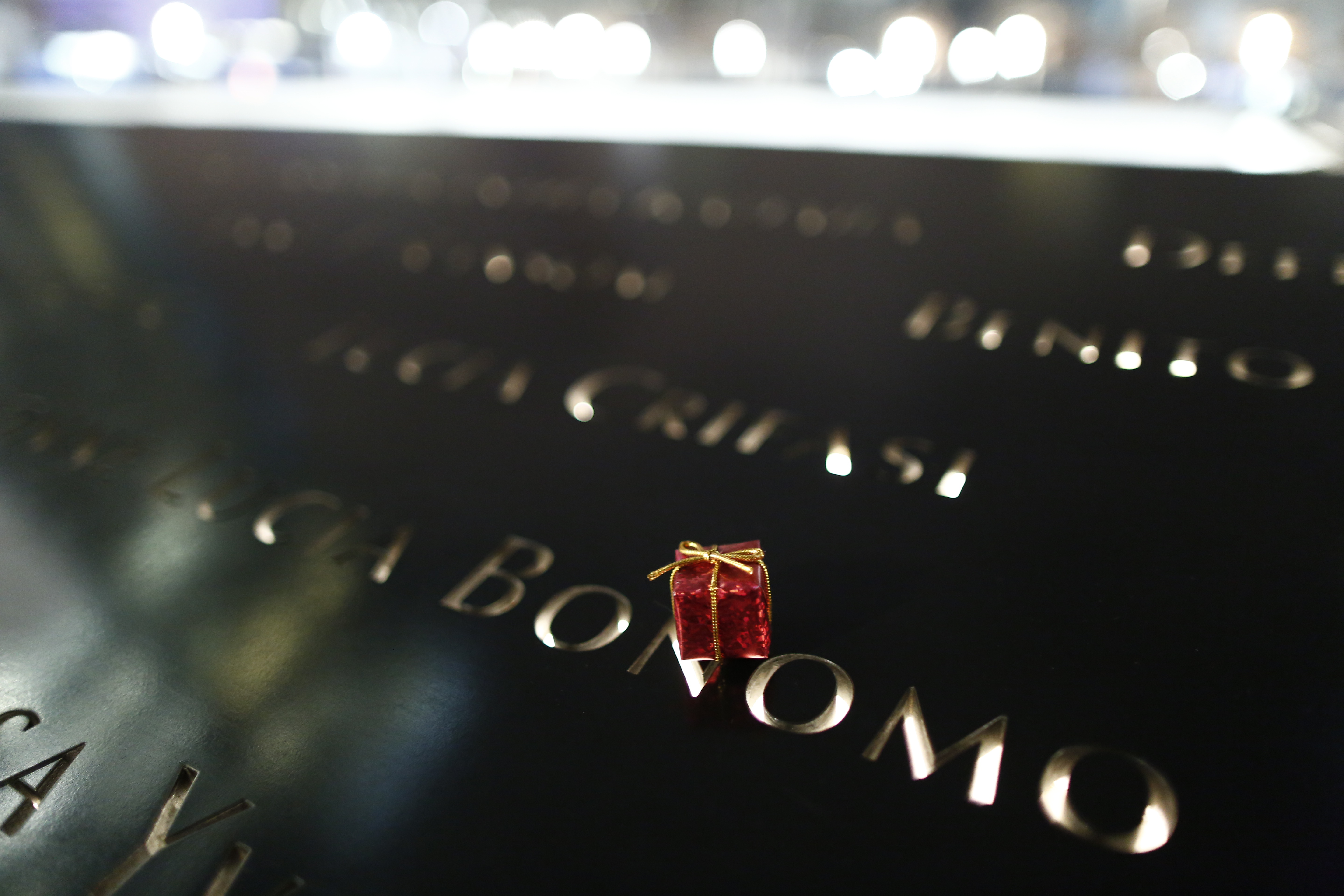 A miniature Christmas gift with red wrapping paper and a gold ribbon has been placed at a name on the 9/11 Memorial.