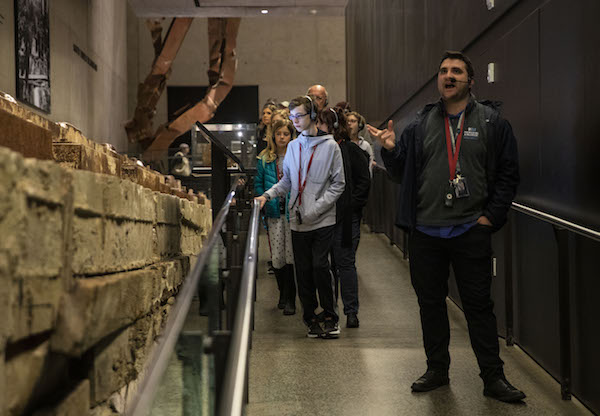 Senior interpretive guide Beau Wilson gestures as he leads a tour of visitors through the Museum. Twisted steel from the Twin Towers is seen in the background.