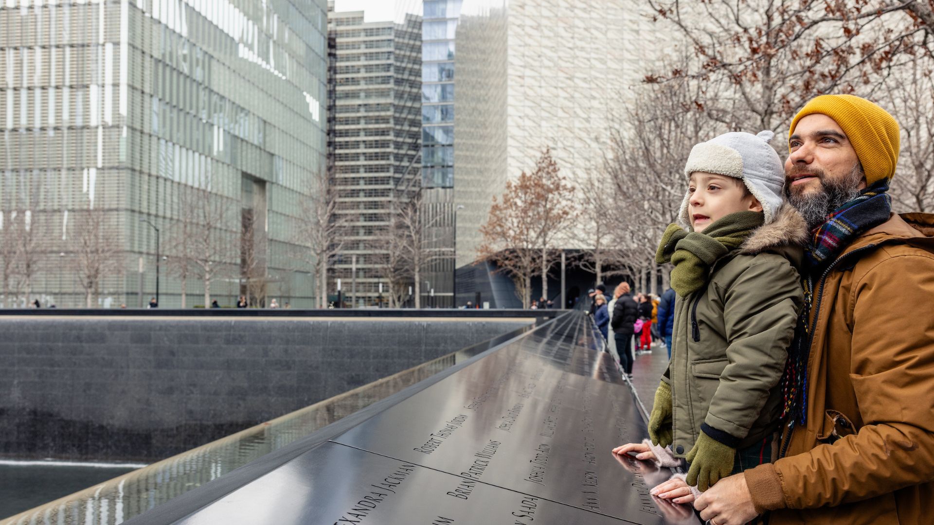 A young boy, propped up by his father, looks out over one of the pools on the 9/11 Memorial.