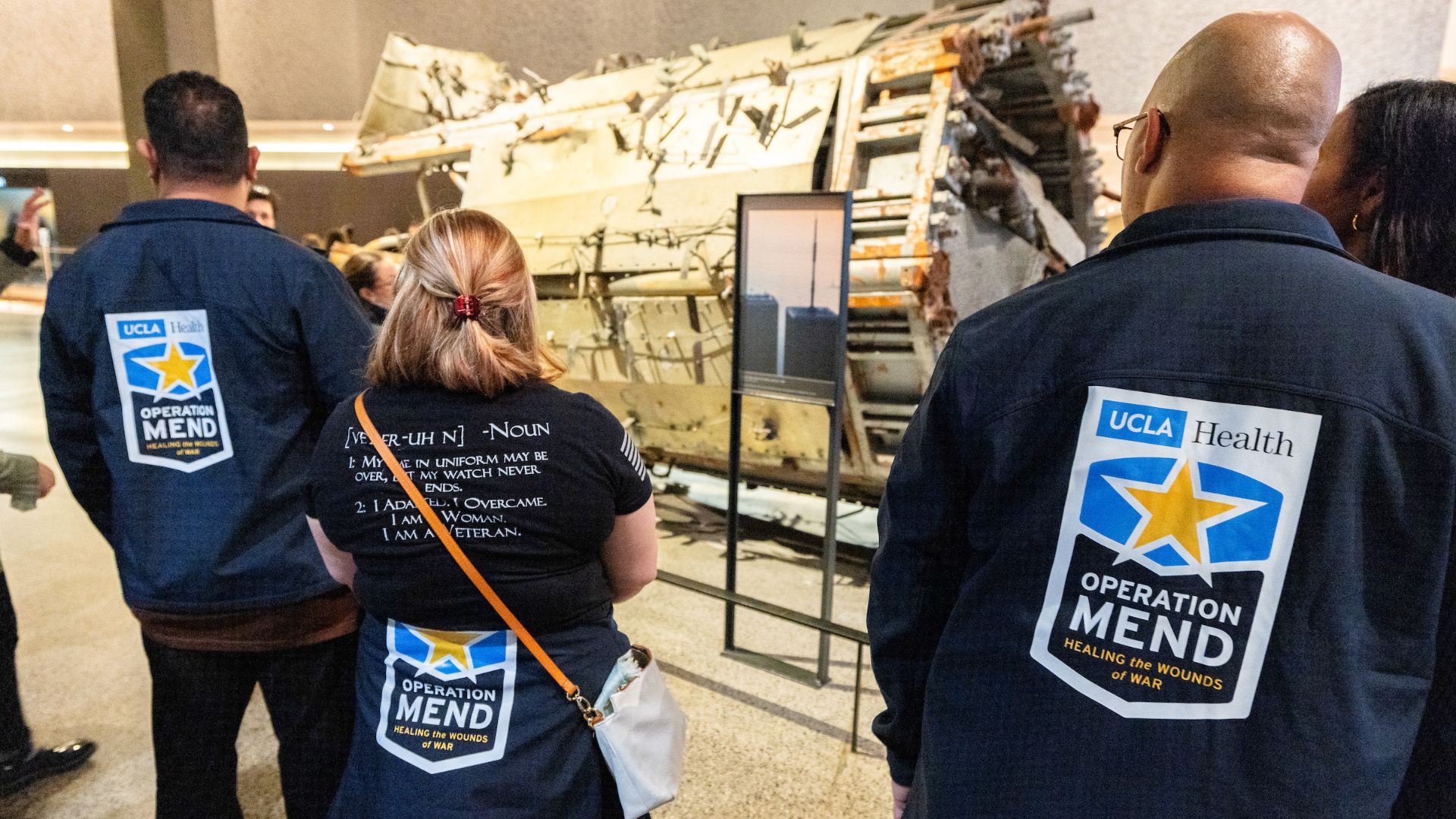 Back view of guests wearing Operation Mend jackets study a large artifact in the museum