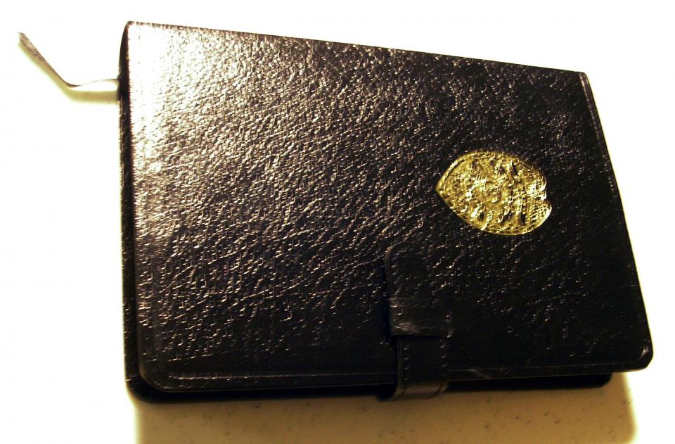A black leather police officer’s bible is displayed on a white surface. It includes a gold police shield on its cover.