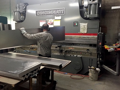 A National employee inserts a large piece of sheet metal into a press brake to bend it into a specified shape.