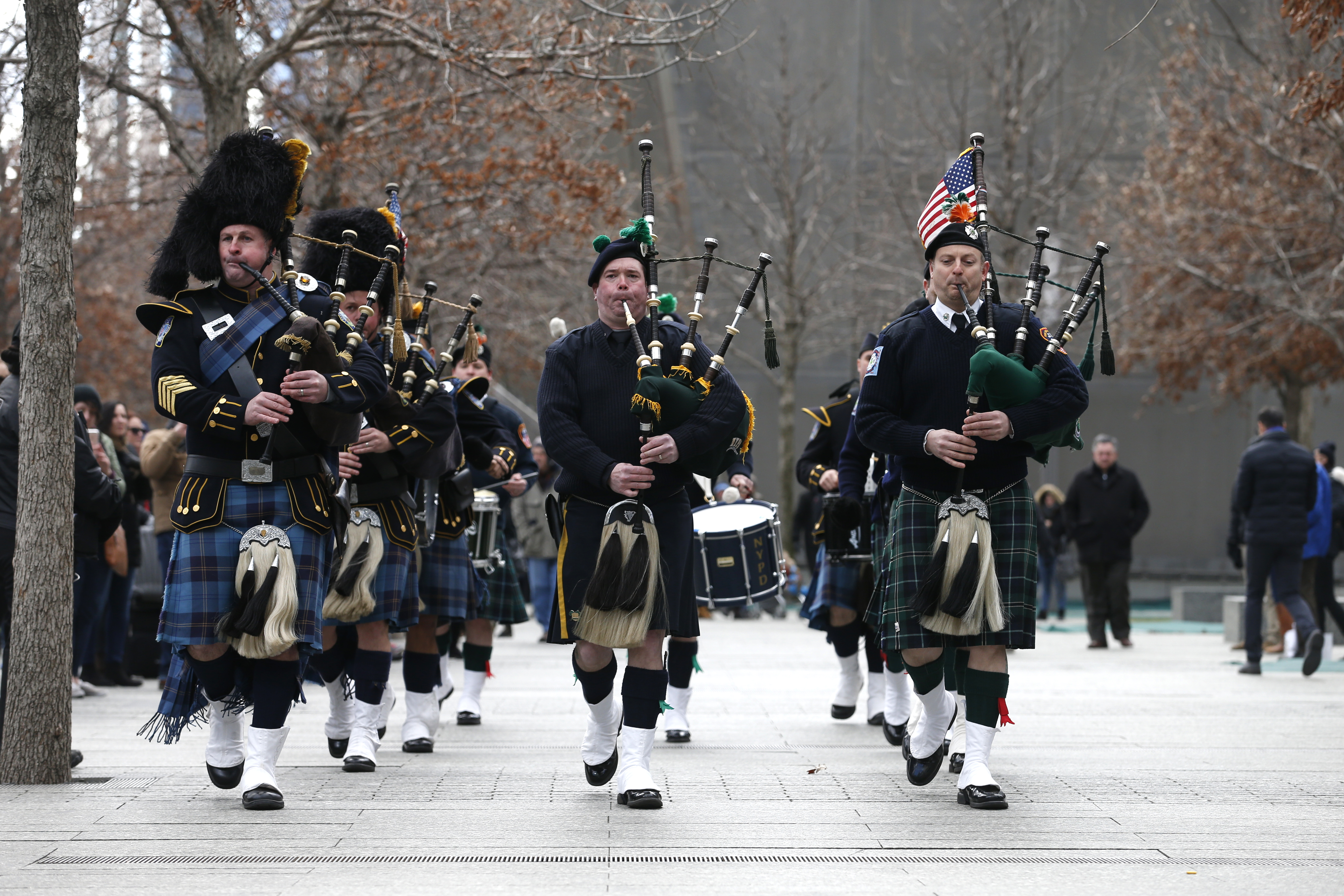 Bagpipe and drum players affiliated with the NYPD and the Port Authority play at the 9/11 Memorial on a cloudy autumn day.