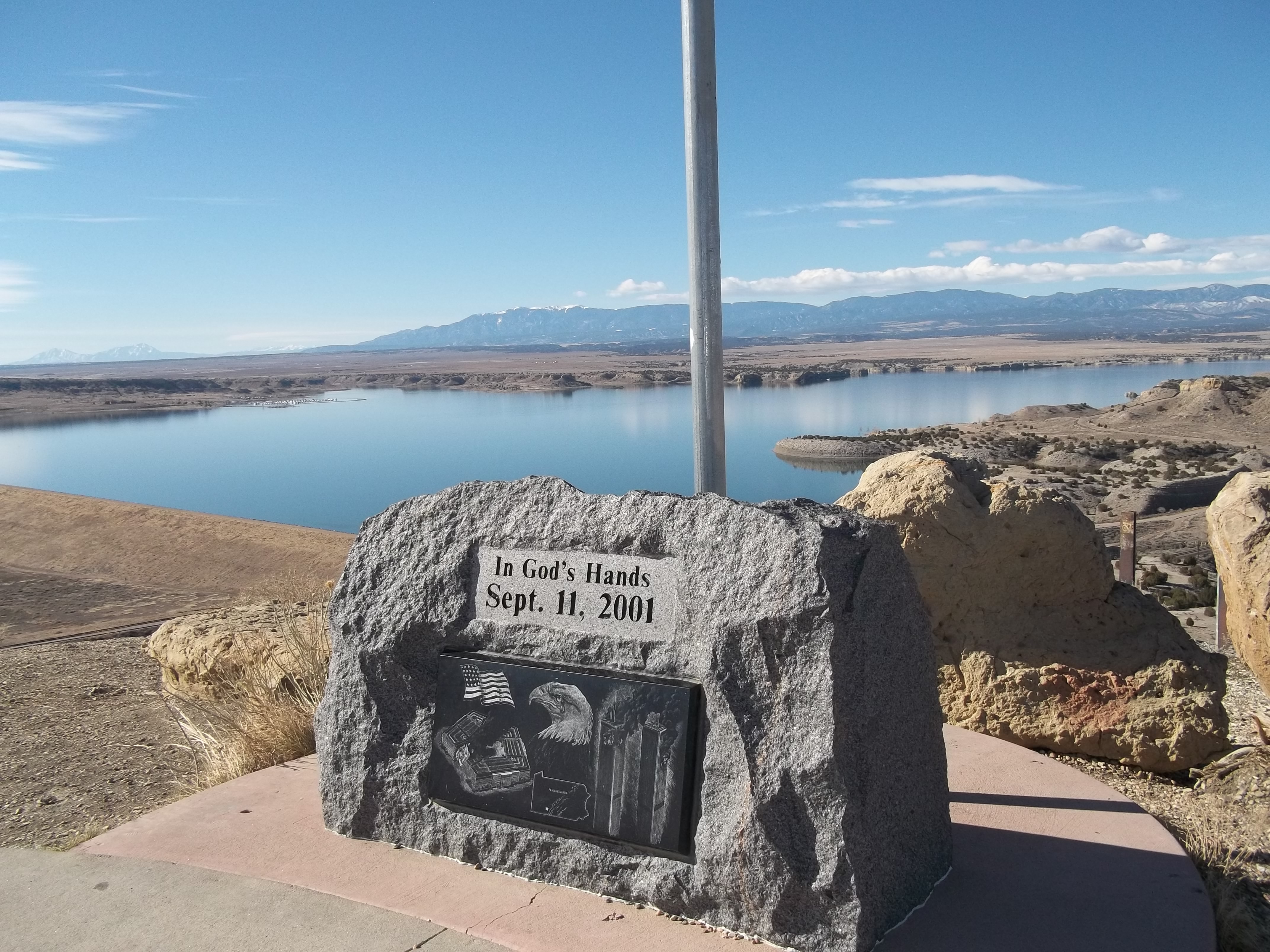 The Liberty Point 9/11 Memorial is seen on a hillside in Pueblo West, Colorado. Mountains and a big blue sky are seen in the background. The memorial reads “In God’s Hands September 11, 2001.”