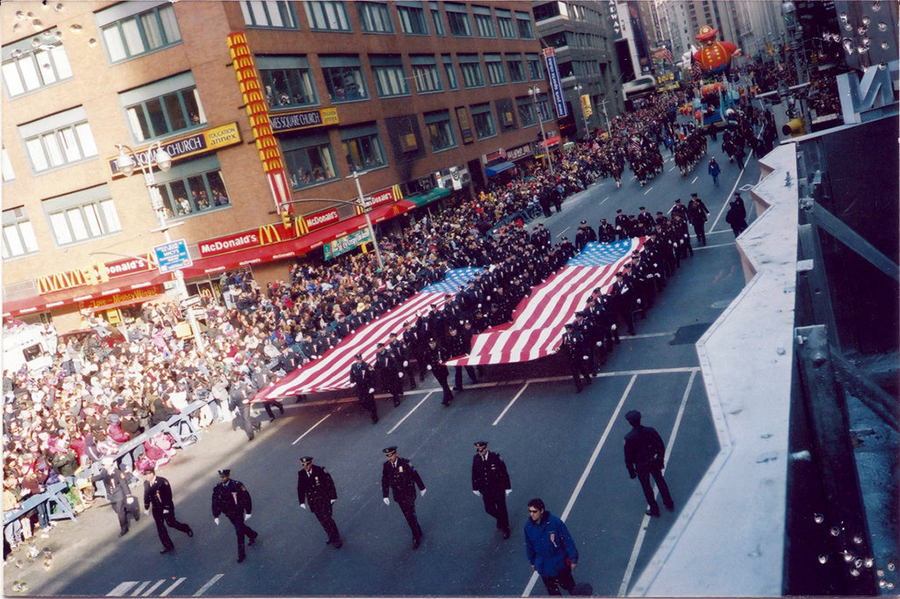 A view over the 2001 Macy’s Thanksgiving Parade shows formally dressed emergency responders carrying two long American flags down an avenue in Manhattan.