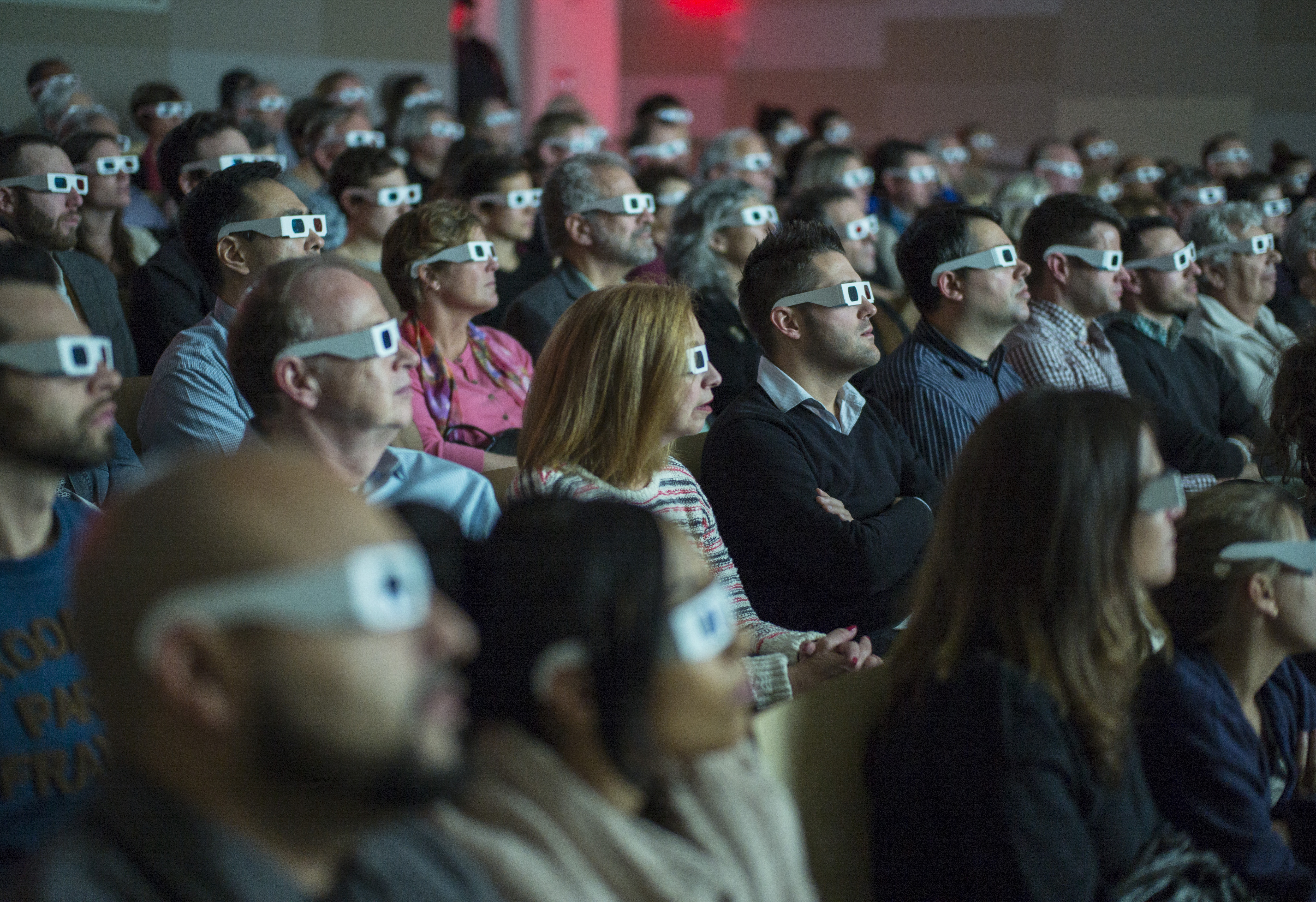 Public program attendees view a 3D video sculpture out of view at the Museum Auditorium. The dozens of audience members are wearing white 3D glasses with red and blue lenses.
