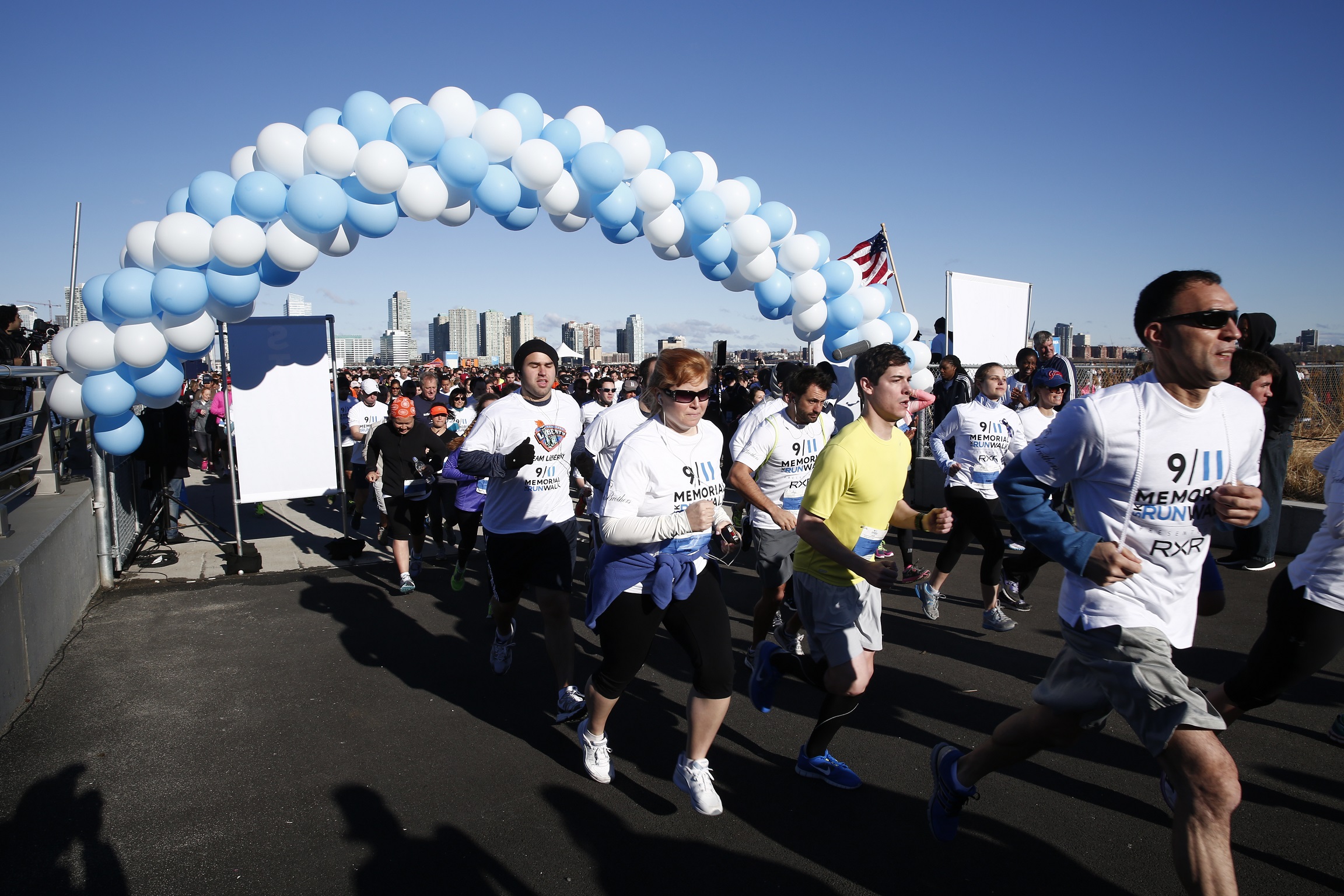 Participants across the finish start line at the 9/11 Memorial 5K Run and Walk in 2014. They pass under an archway made of white and blue balloons.
