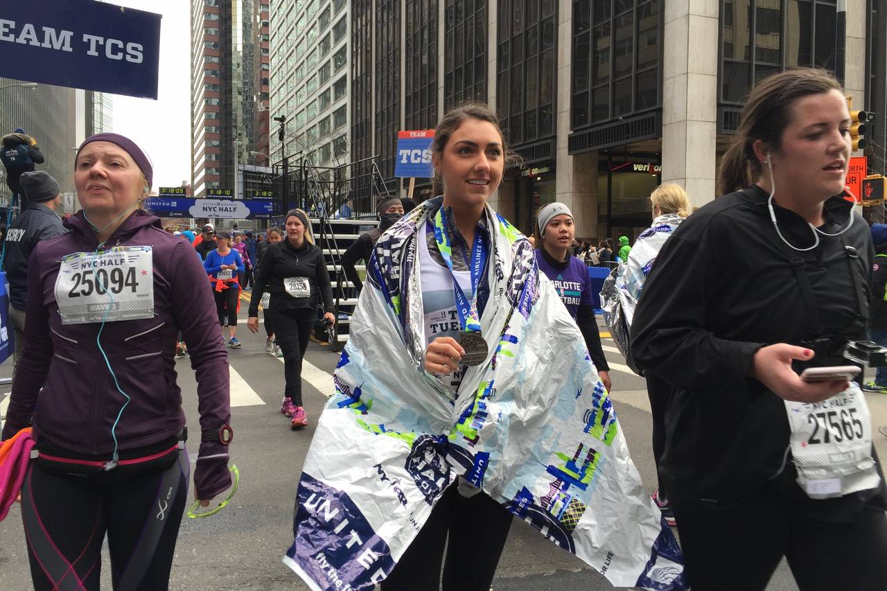 Katelyn Mascali shows of a medal that’s around her neck as she takes part in the New York City Half Marathon. She is surrounded by other runners taking part in the event.
