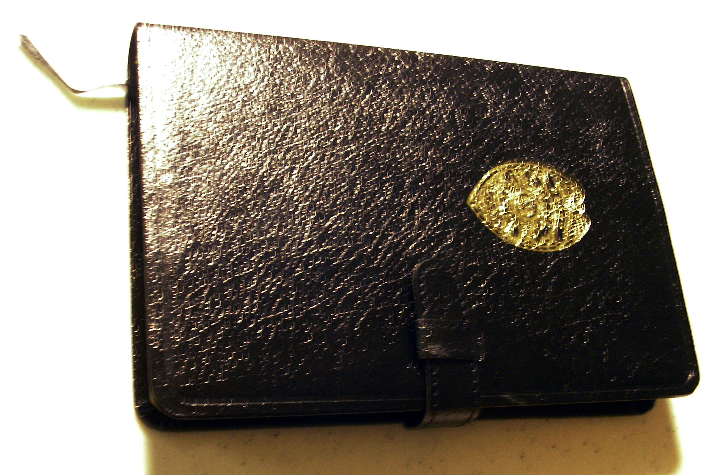 A black leather police officer’s bible is displayed on a white surface. It includes a gold police shield on its cover.