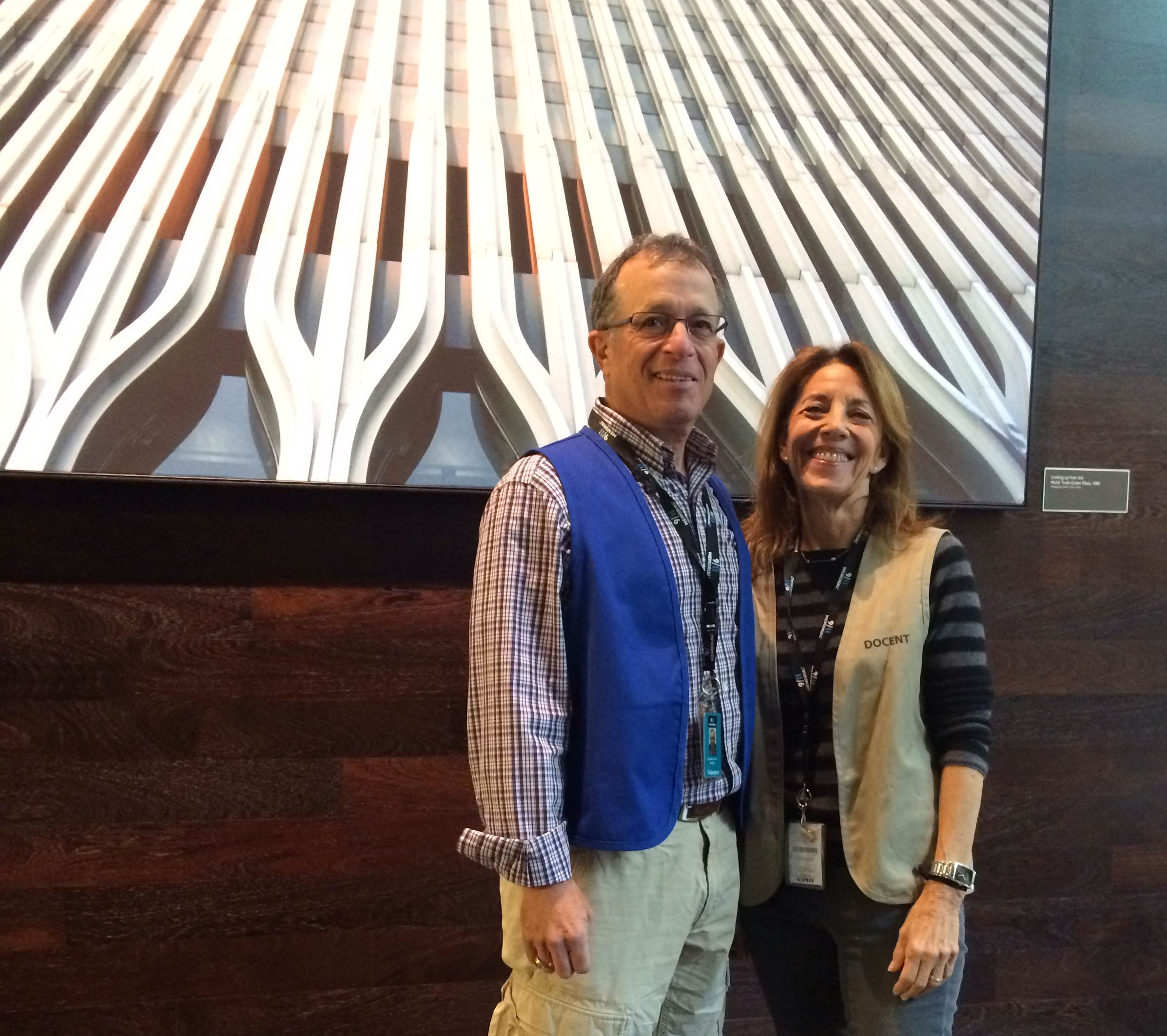 Ellen and Doug Burns, both volunteers at the 9/11 Memorial Museum, stand in front of a poster-sized, framed image of the Twin Towers.