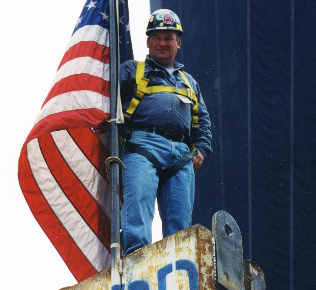 William Quindlan stands atop the Last Column at Ground Zero. He is holding onto an American flag that has been placed on top of the column.