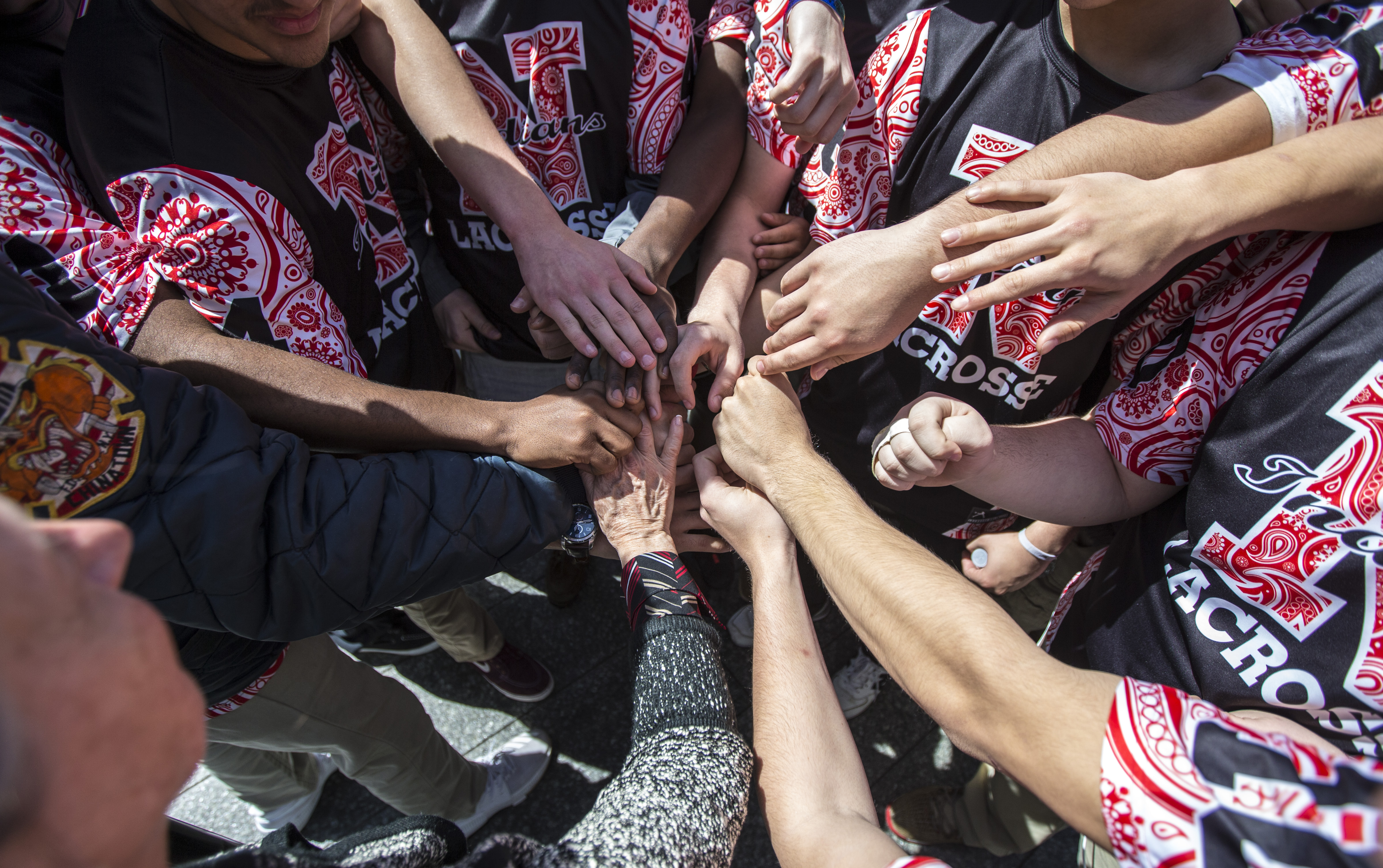 Members of the Nyack Boys varsity lacrosse team put their hands together in a circle while visiting Memorial plaza.