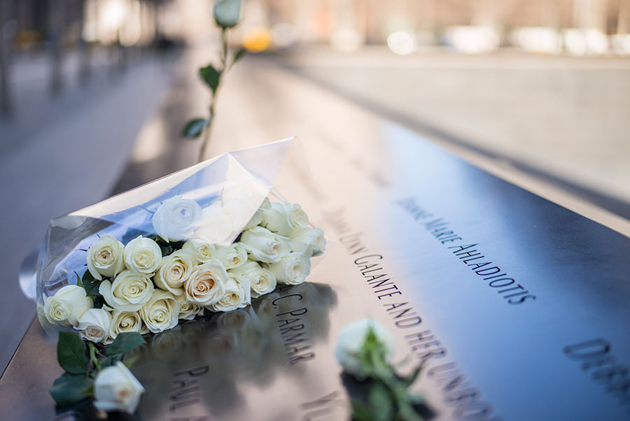 A bouquet of white roses has been left at a name on the 9/11 Memorial. A single yellow rose is seen placed at a name in the background.