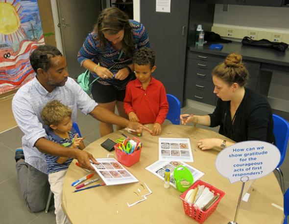 A man, woman, and two boys take part in an activity for families at the Museum’s Education Center. A woman who works at the Museum assists the boys as they work on an art project around a circular table.