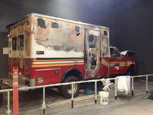 A damaged FDNY ambulance from 9/11 is seen at the Museum before its opening. The top and sides of the ambulance are burned and the front of it is heavily damaged.