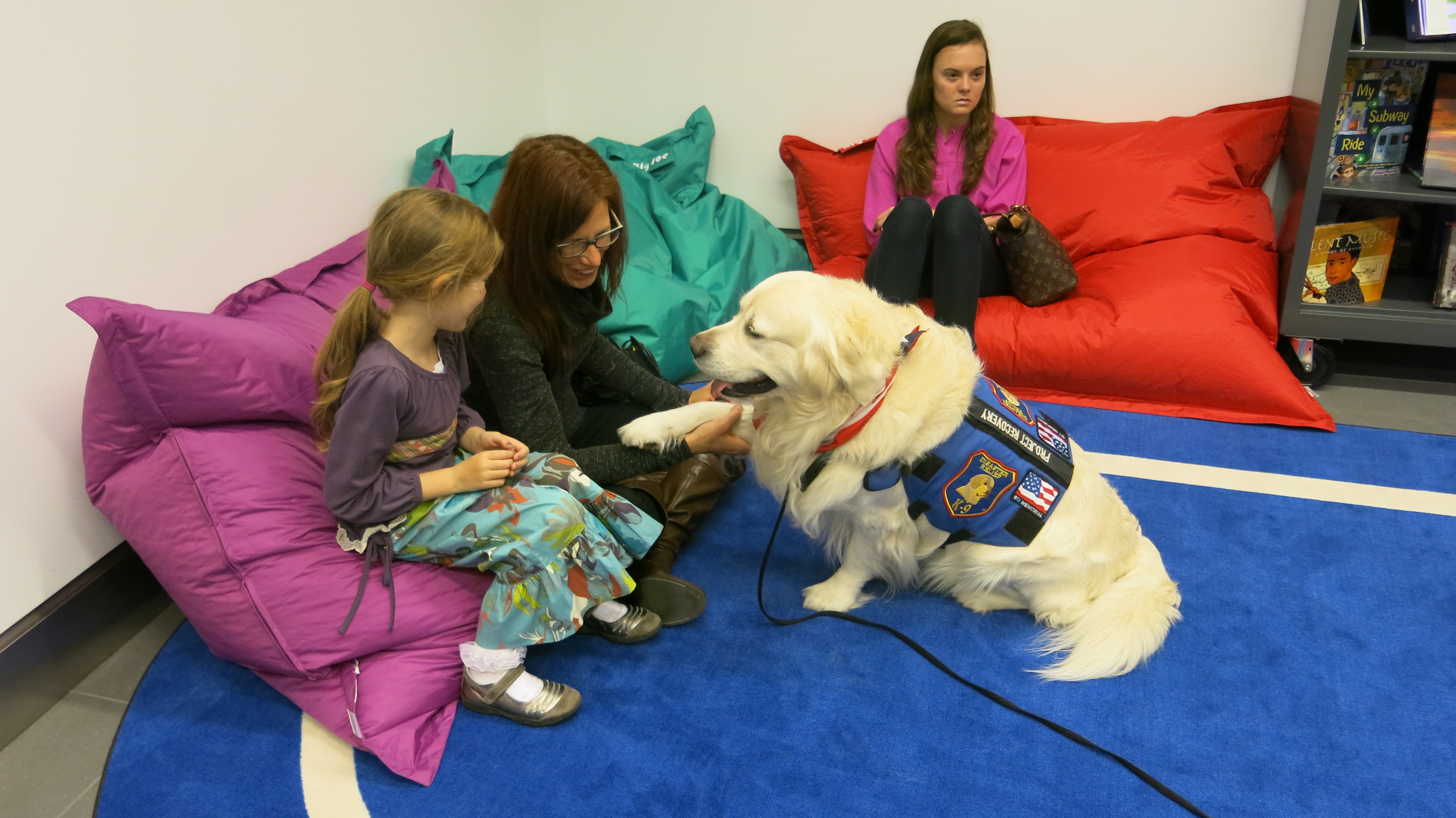 A girl and a woman pet the comfort canine Chance while seated on bean-bag pillows at the Museum.
