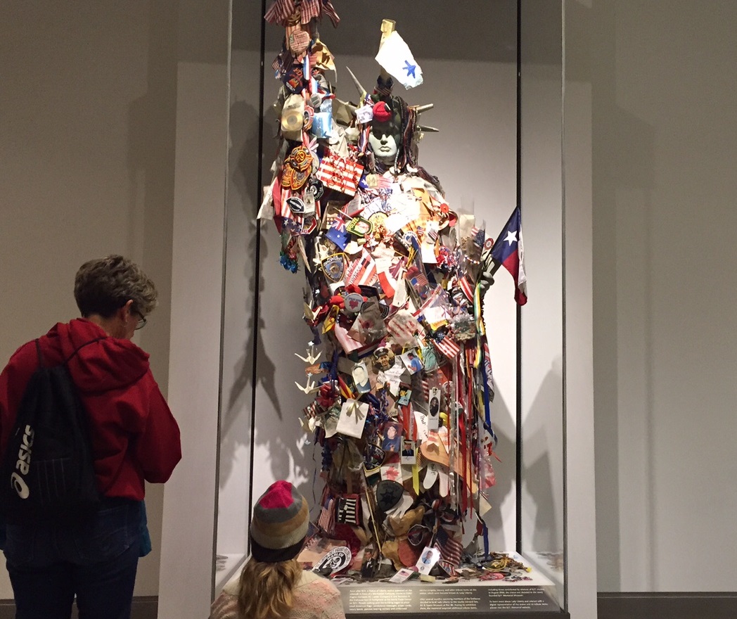 Museum visitors look at the Lady Liberty sculpture at the 9/11 Memorial Museum. The sculpture, a reproduction of the Statue of Liberty, is covered in tributes like flags and photos.