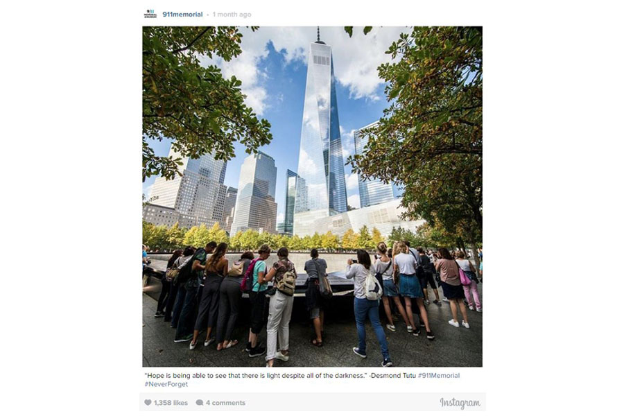 A screenshot of an Instagram post shows visitors gathered around a Memorial reflecting pool on a sunny day. One World Trade Center towers over them in the distance. Blue sky and clouds reflect off the building and other buildings nearby.