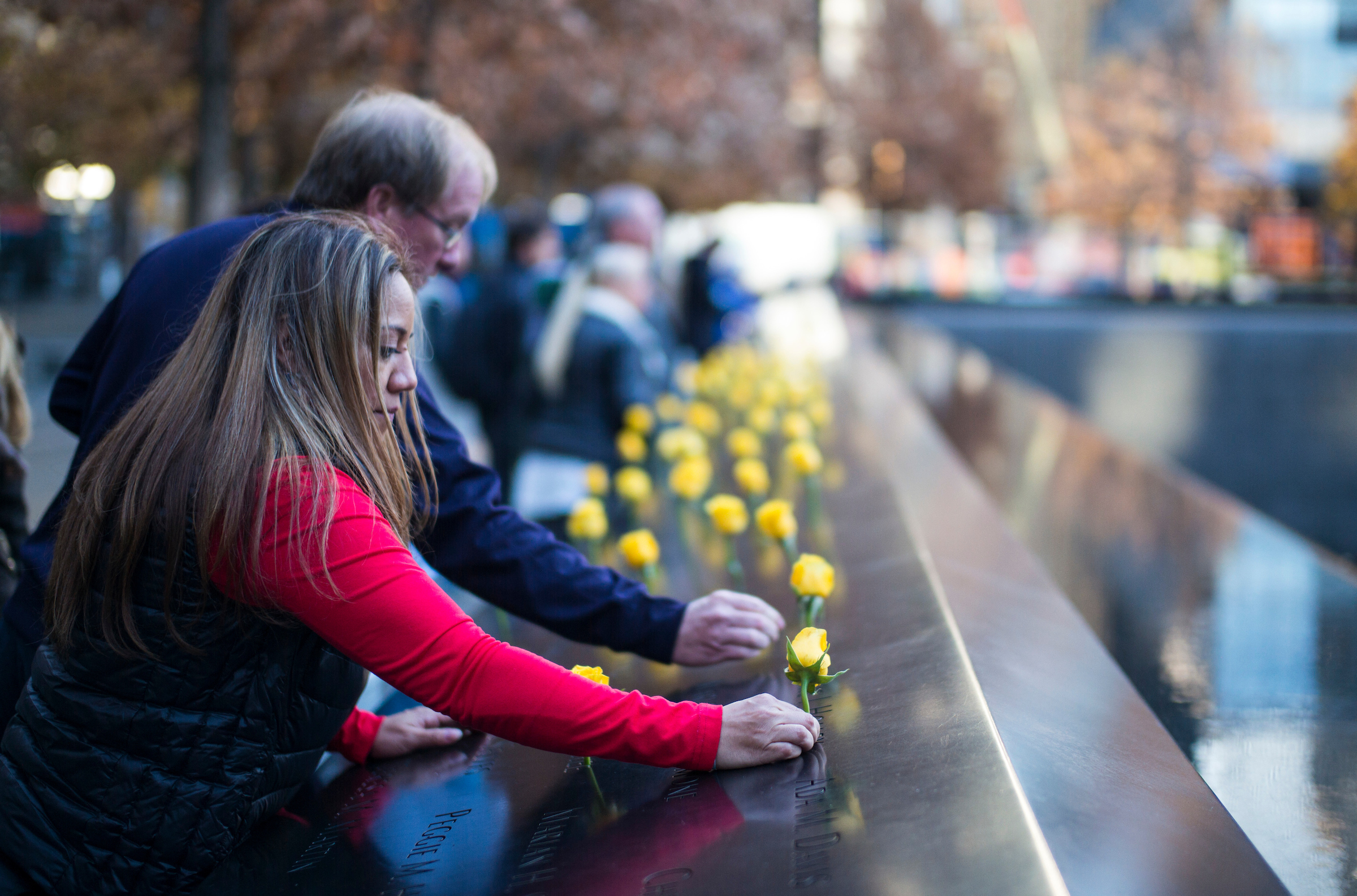 A man and a woman place yellow roses on the 9/11 Memorial for Veterans Day.