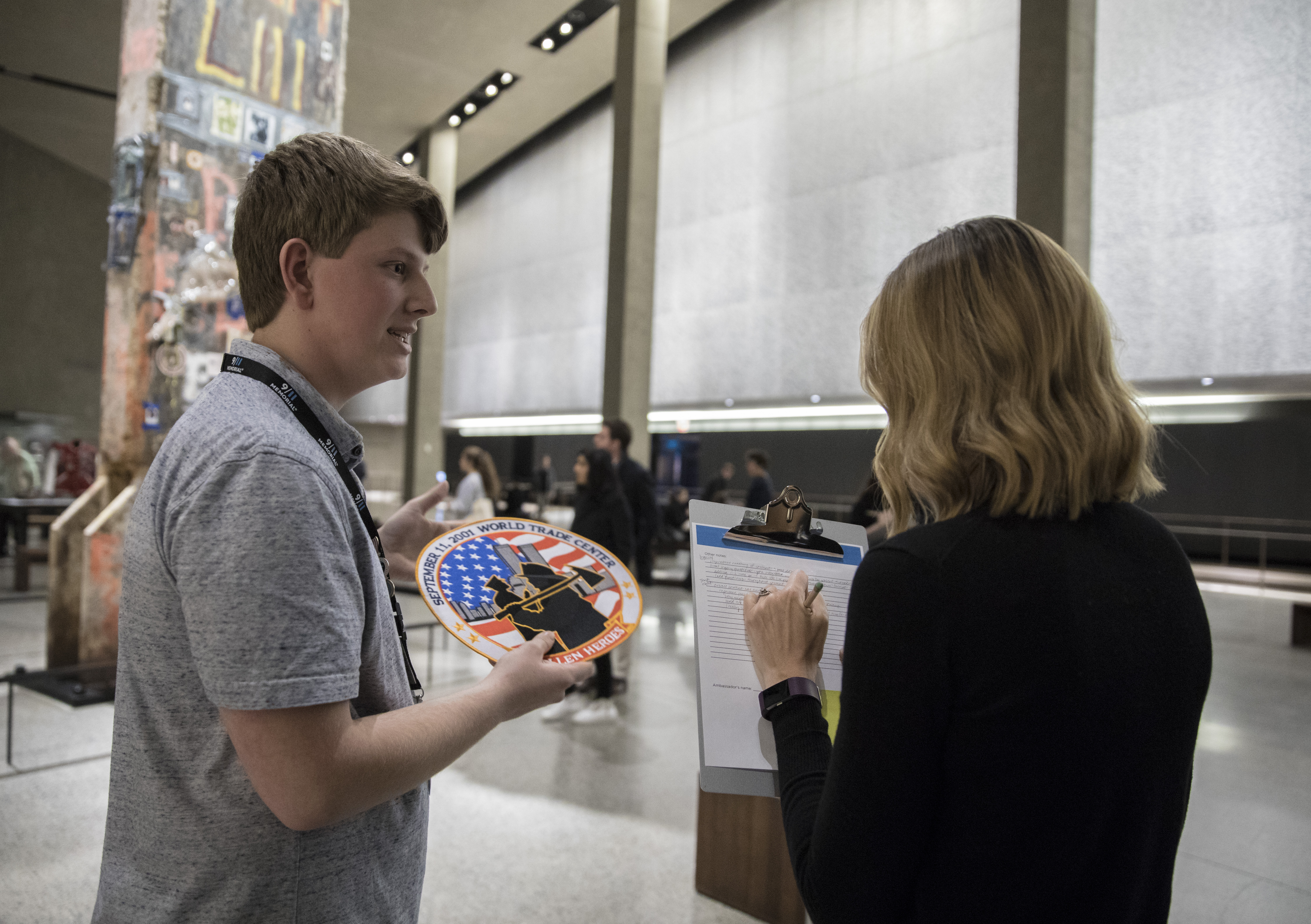 John Spade, son of 9/11 survivor and museum docent, Bill Spade, speaks to a woman with a clipboard beside the Last Column in Foundation Hall. He is holding up a large patch dedicated to the heroes of 9/11.