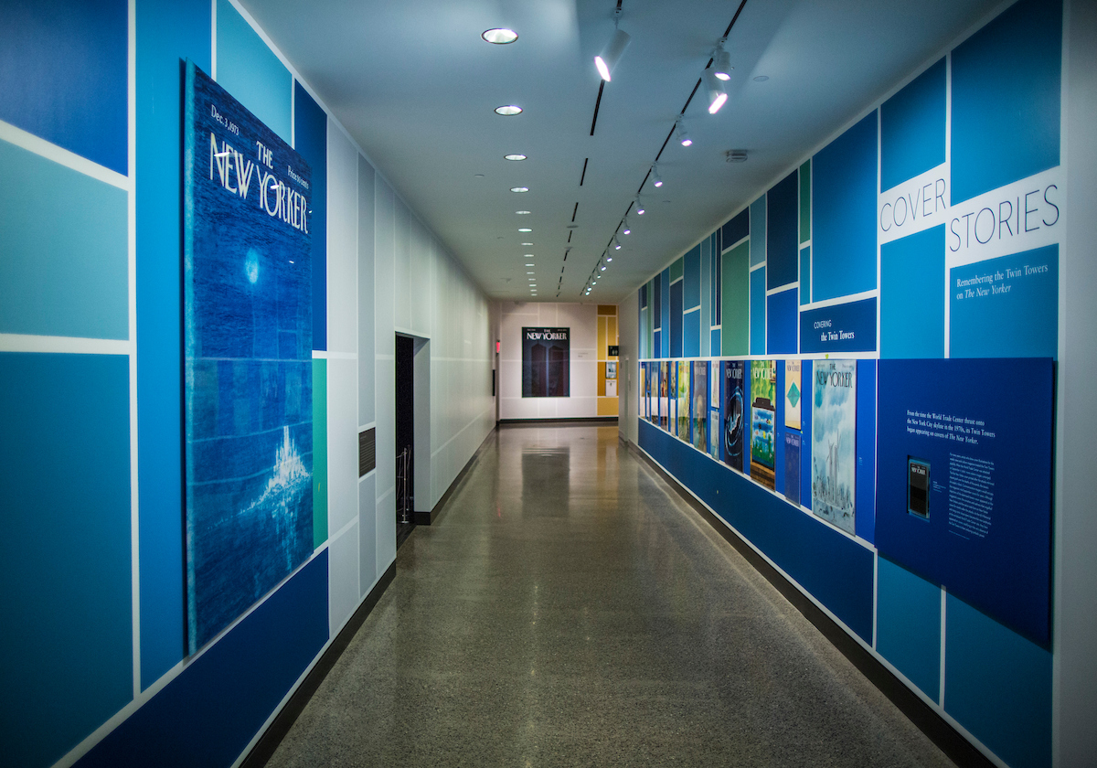 The exhibition “Cover Stories: Remembering the Twin Towers on The New Yorker” is seen in a part of the Museum. Covers from past New Yorker issues are prominently displayed along two walls and on a distant wall.