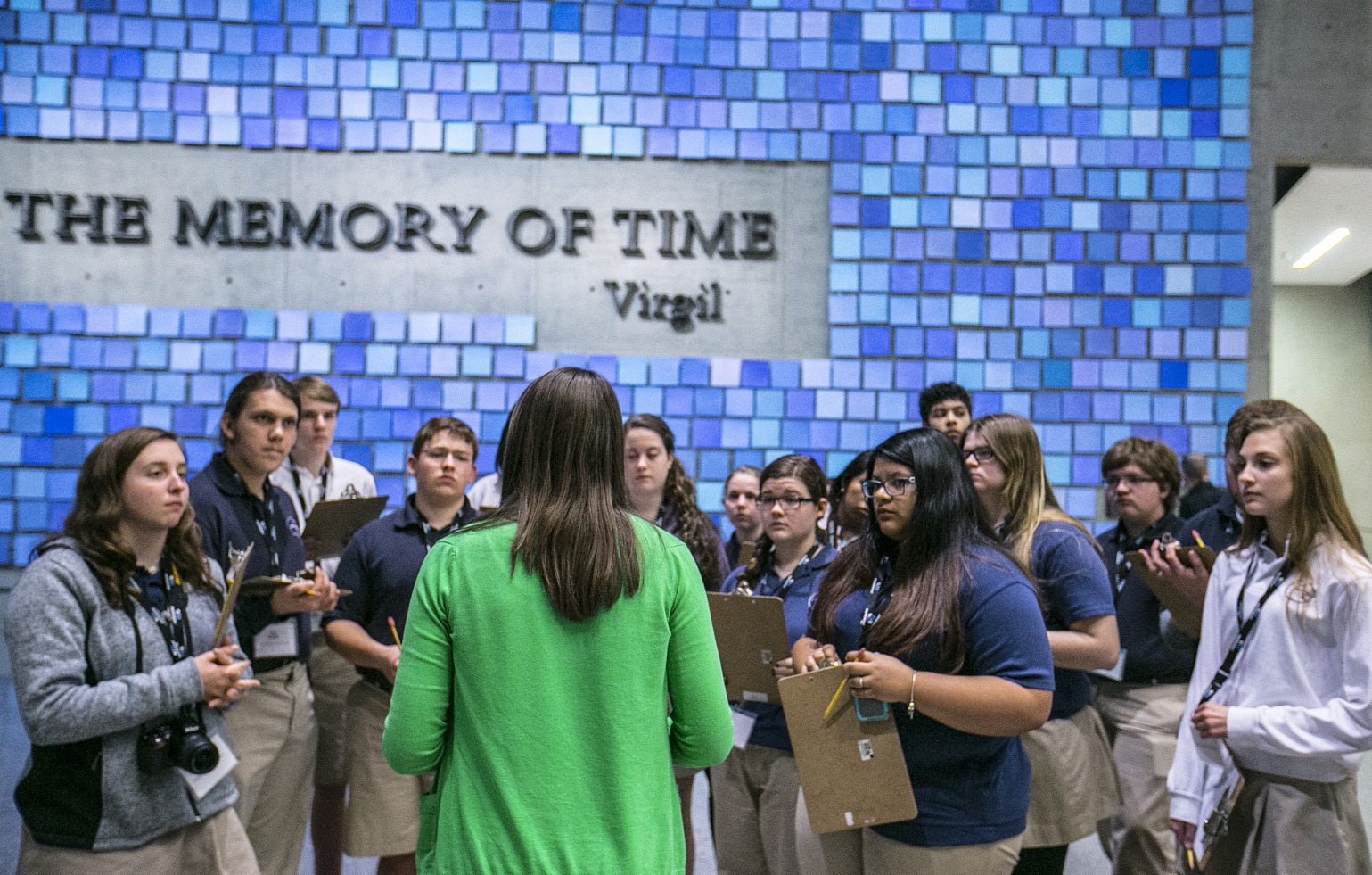 A group of teenage students listen to a woman while taking part in an education program in memorial hall. The blue tiles of artist Spencer Finch’s installation “Trying To Remember the Color of the Sky on That September Morning” are seen in the background.