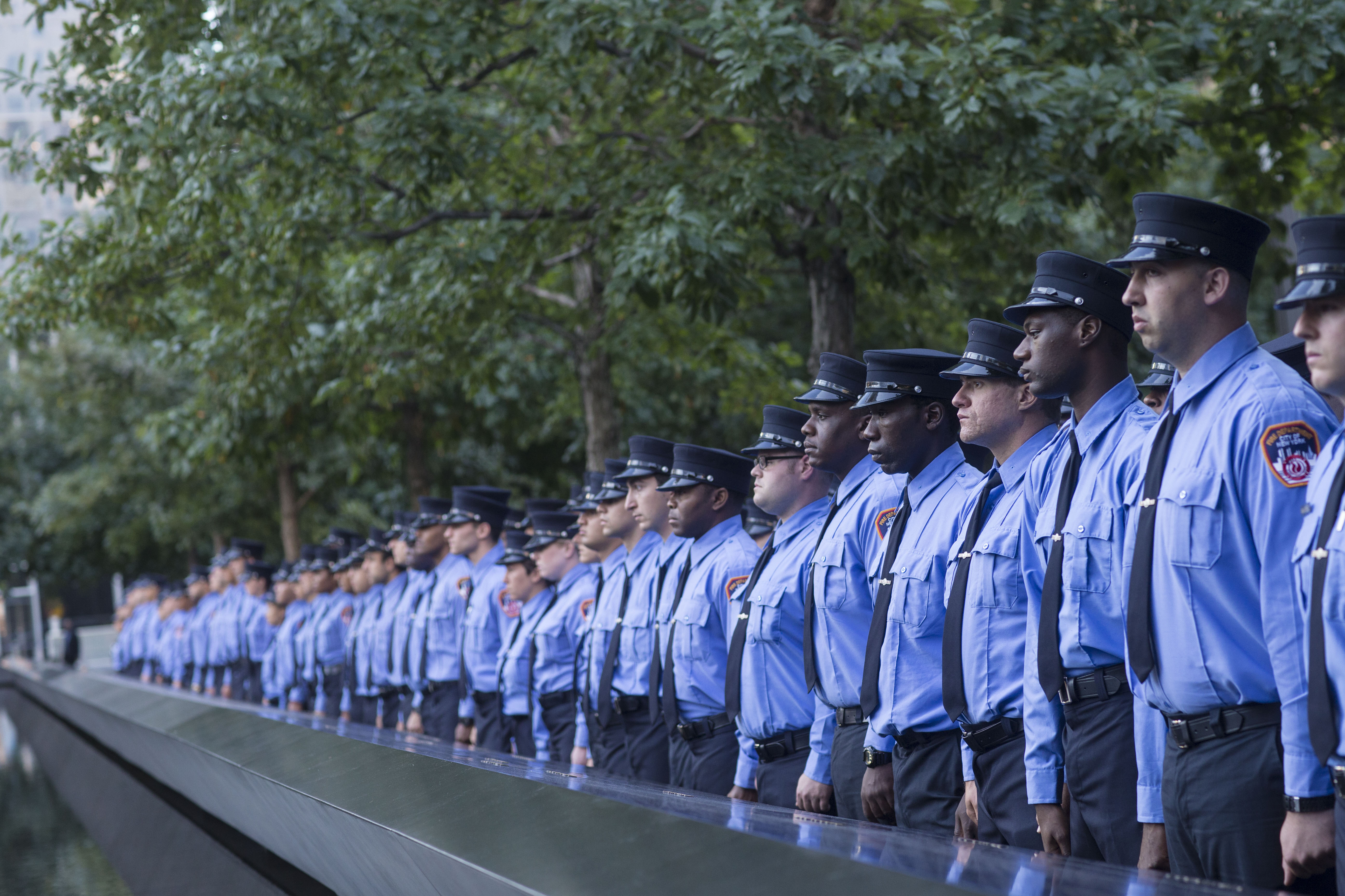A probationary class of FDNY EMTs stands in front of a reflecting pool at the 9/11 Memorial.