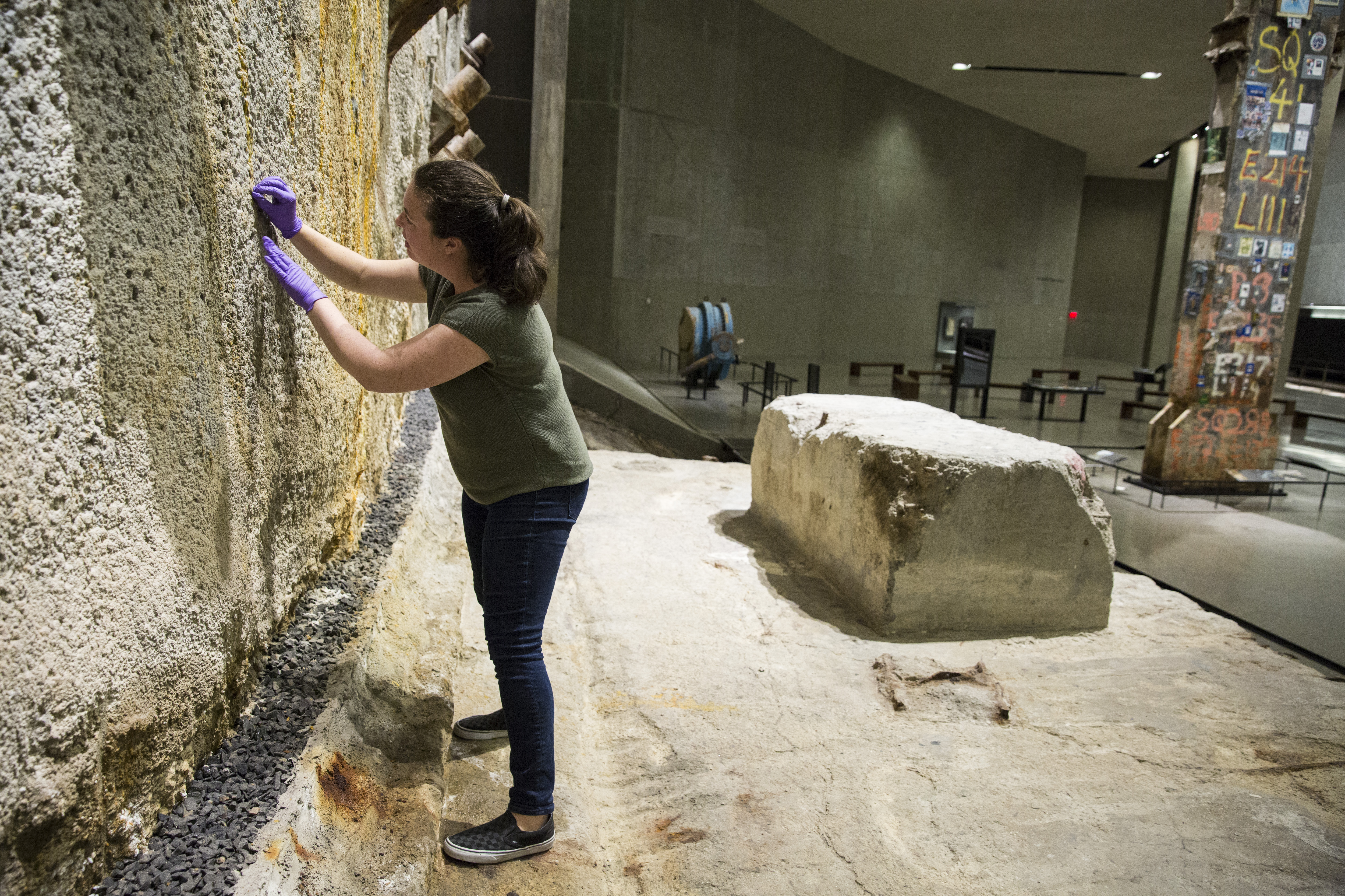 A woman wears purple gloves as she does work conserving the slurry wall at Foundation Hall in the Museum.