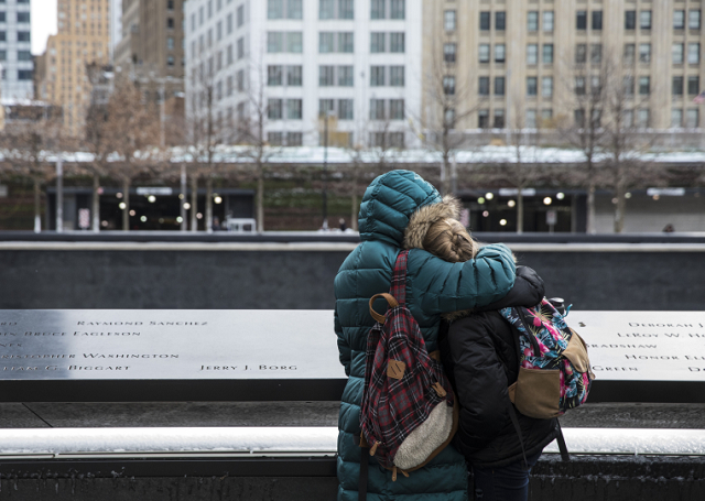 Two visitors dressed in winter jackets embrace beside a name on the Memorial. 