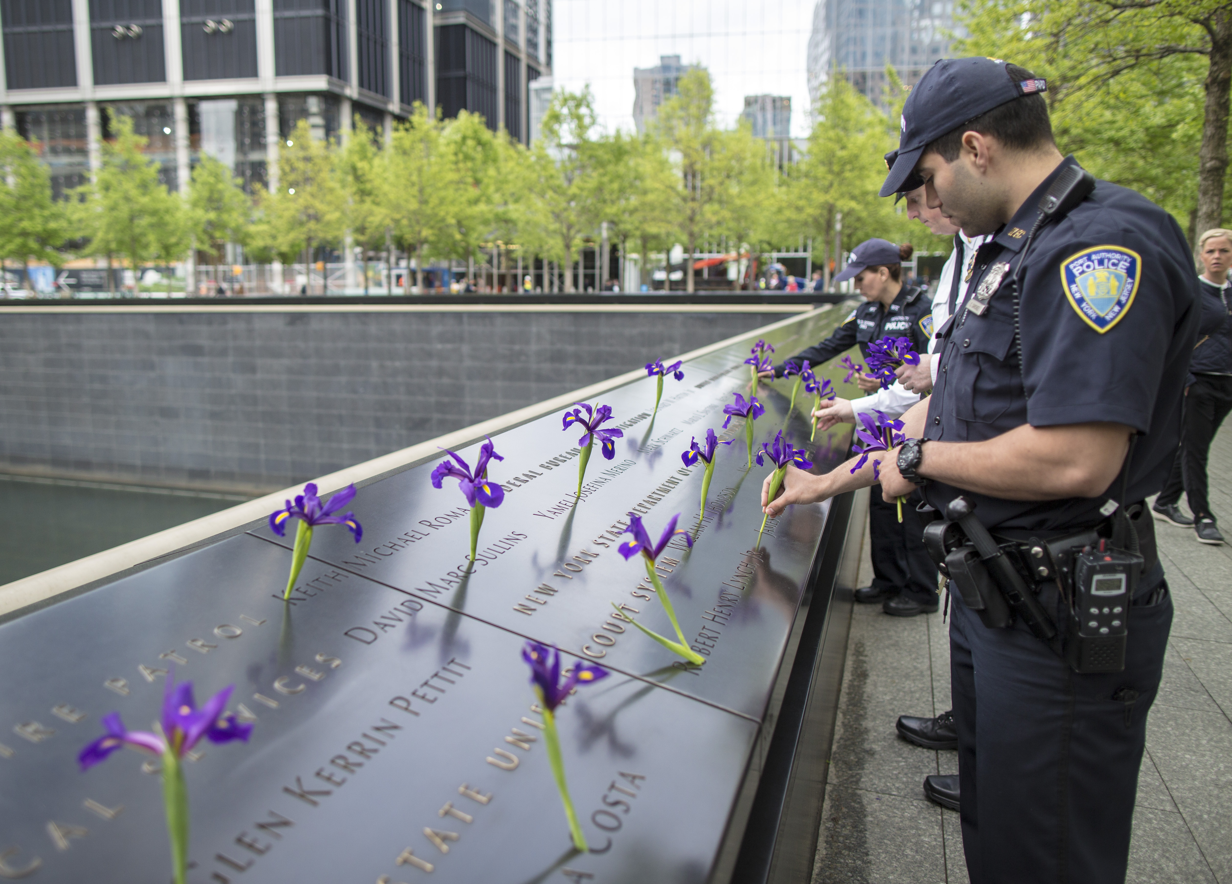 Two uniformed members of the PAPD place purple flowers on a bronze parapet at the Memorial.
