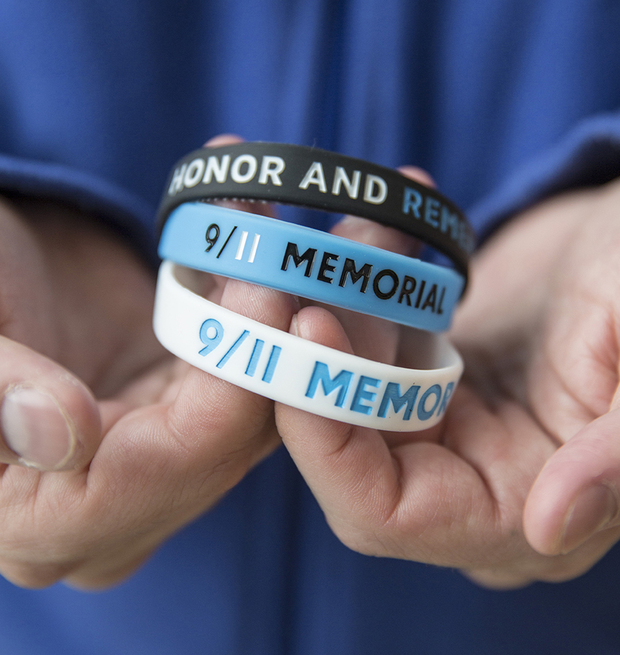 A person’s hands hold up three 9/11 Memorial & Museum bracelets—one of them black, one blue, and one white.