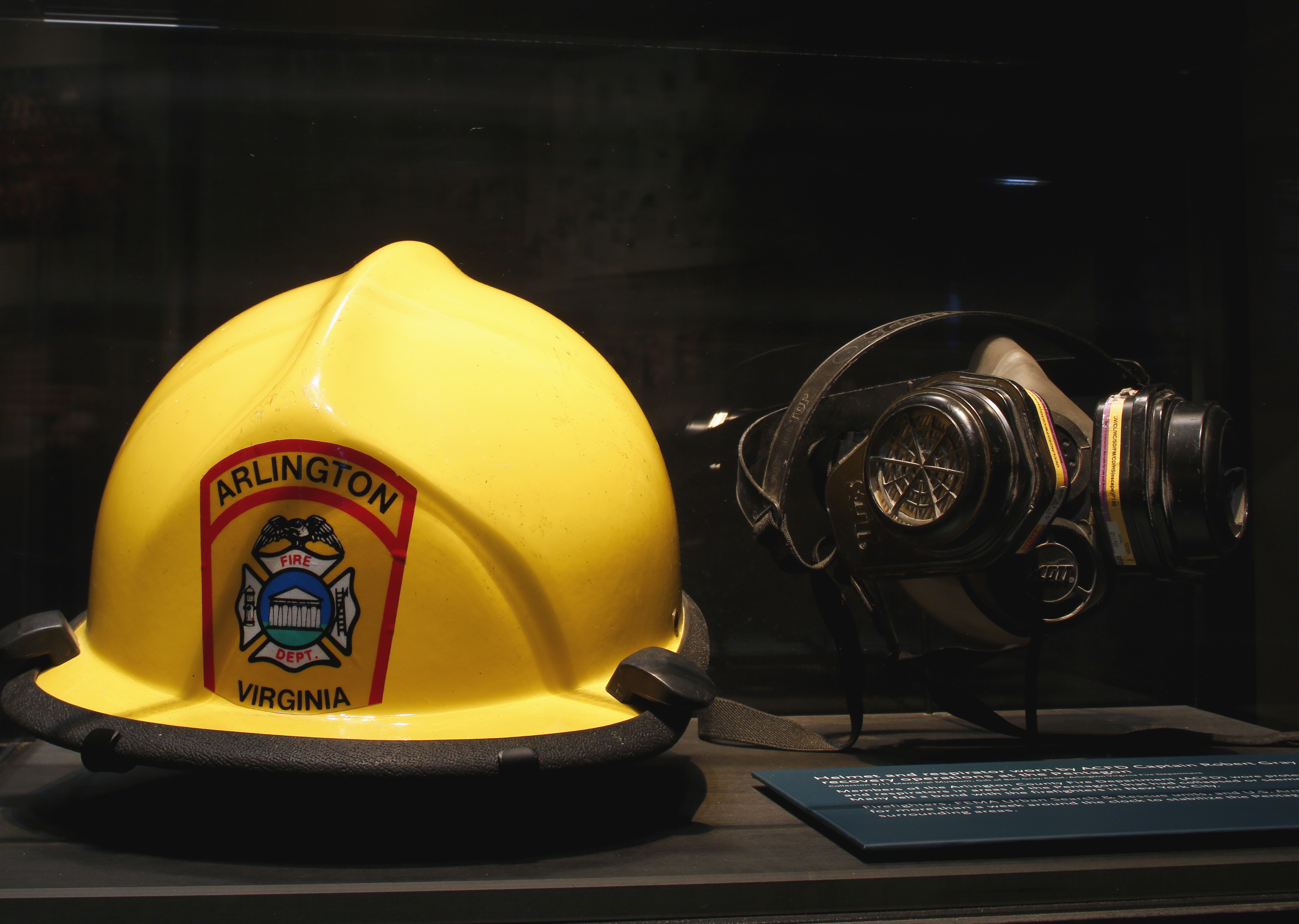 A helmet and respirator are seen in a glass display case at the Museum. The yellow helmet reads Arlington, Virginia, Fire Department.
