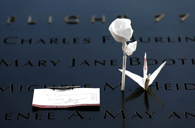 An origami rose and bird and a note have been placed at a name on a bronze parapet at the 9/11 Memorial.