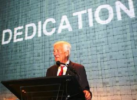9/11 Memorial Founding Chairman John C. Whitehead speaks at a podium. The word “dedication” is projected on a wall behind him.