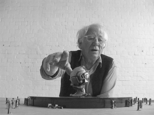 A black and white photo shows Fritz Koenig gesturing near a miniature version of the sphere.
