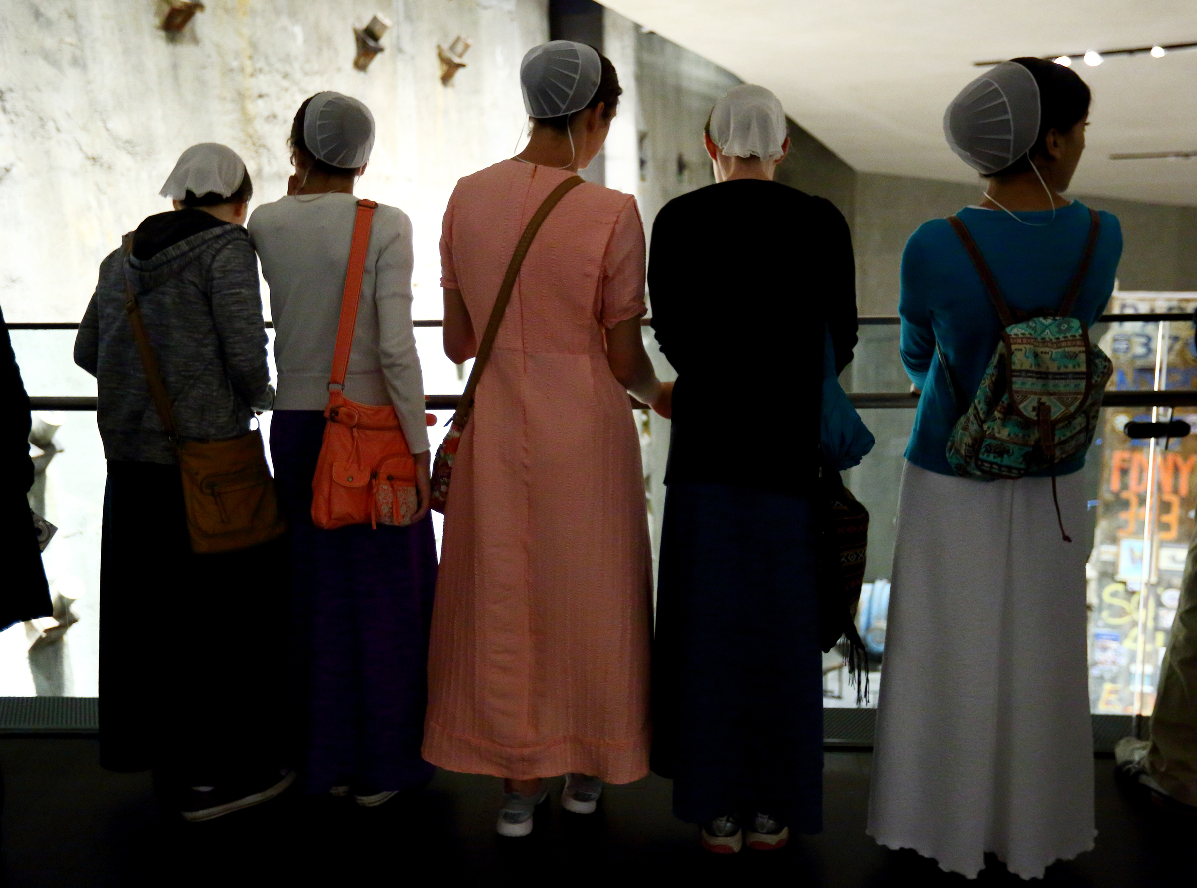Five women in traditional Mennonite dresses look down from the ramp in Foundation Hall to view the slurry wall and Last Column.