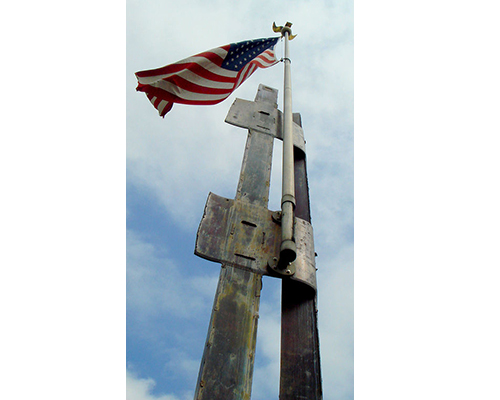 Beams from the North Towers of the World Trade Center rise up to the sky. An American flag is attached to them.