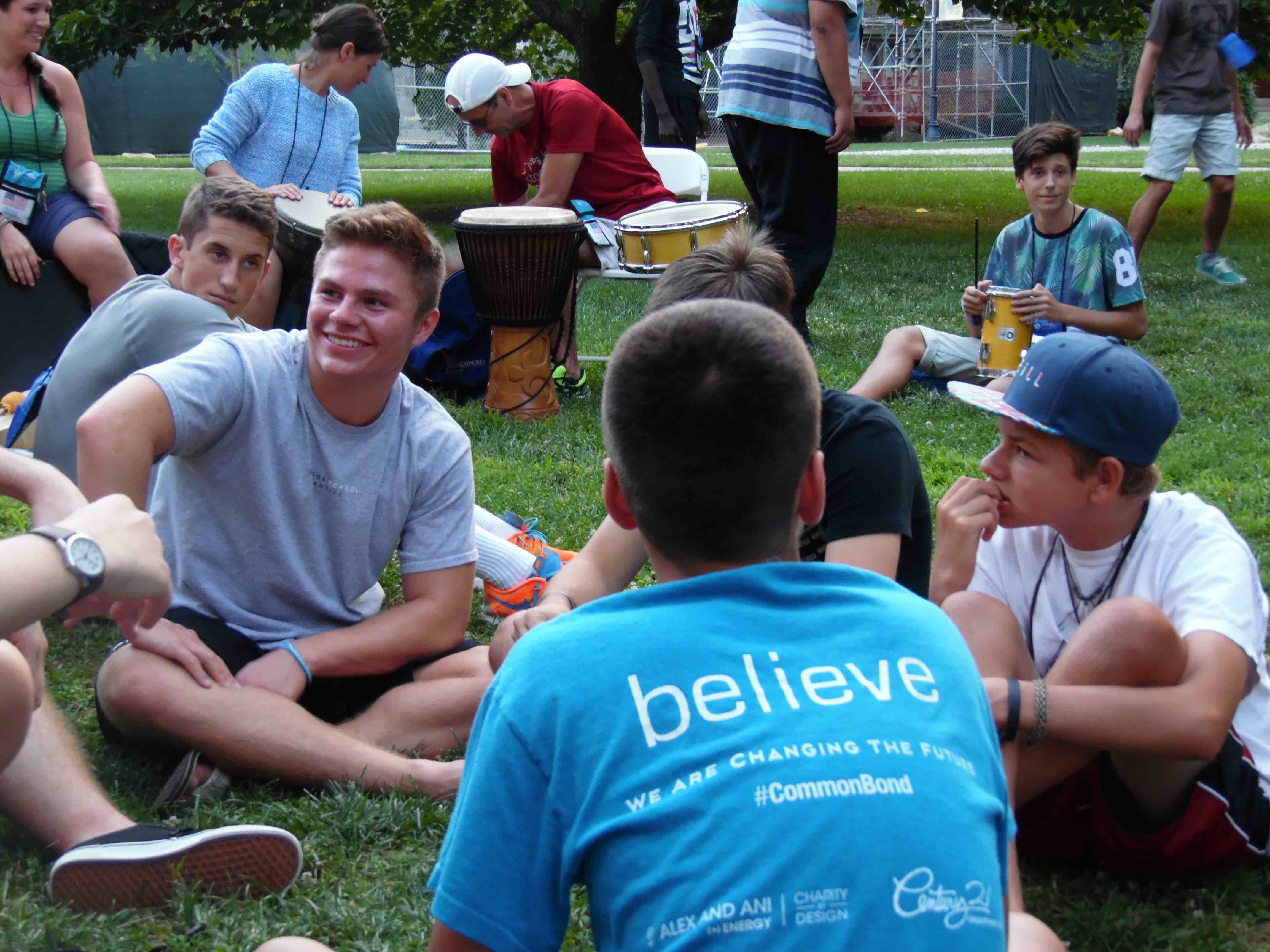 A group of teen boys who have experienced a loss due to terrorism sit together on a grassy area.