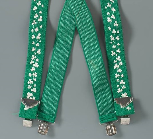 Green suspenders belonging to FDNY Lieutenant Michael Quilty are displayed on a gray surface. The suspenders include designs of shamrocks.