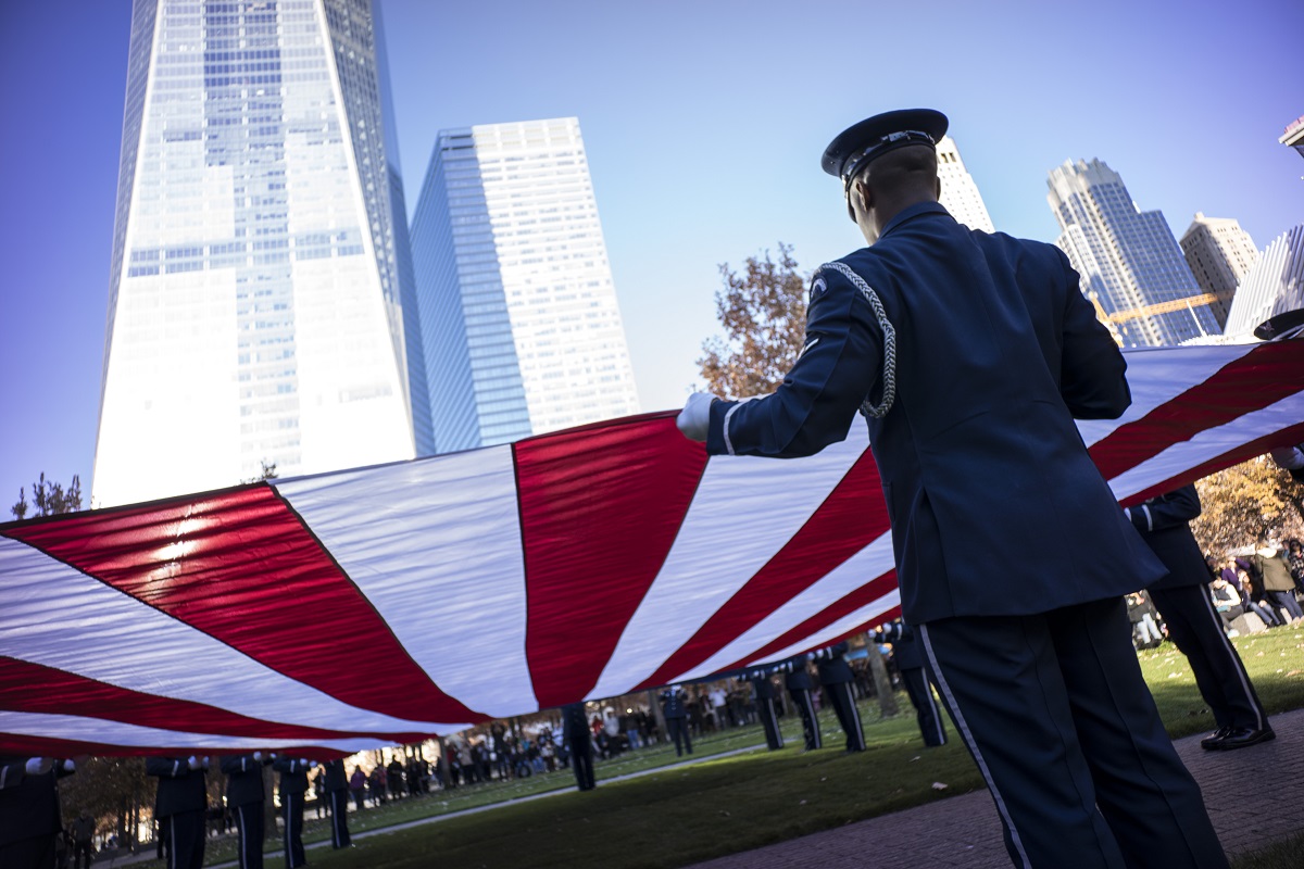 The U.S. Air Force Honor Guard folds a large American flag at the 9/11 Memorial. One World Trade Center towers over them.