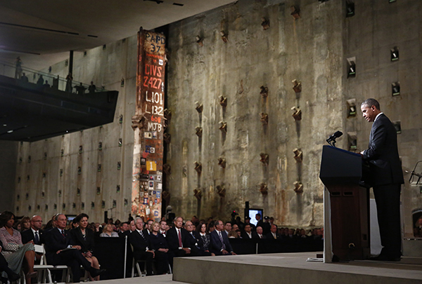 President Barack Obama speaks at a podium onstage at the Museum’s Foundation Hall. Members of the audience watch on in front of the Last Column and Slurry Wall. Among them is Michelle Obama, Michael Bloomberg, Bill Clinton, Hillary Clinton, and George Pataki.