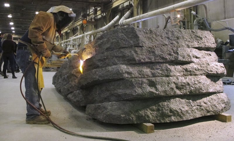 A masked worker from Rock of Ages uses a blowtorch to fuse a granite monolith for the 9/11 Memorial Glade.
