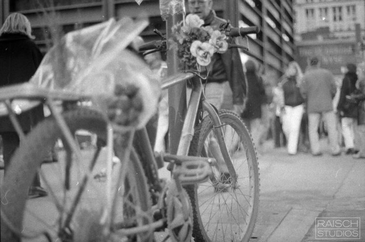 In this black-and-white photo from 2001, a delivery bicycle is seen chained to a pole near the World Trade Center site. The bike is covered in flowers and other items memorializing the owner who never returned to claim it.