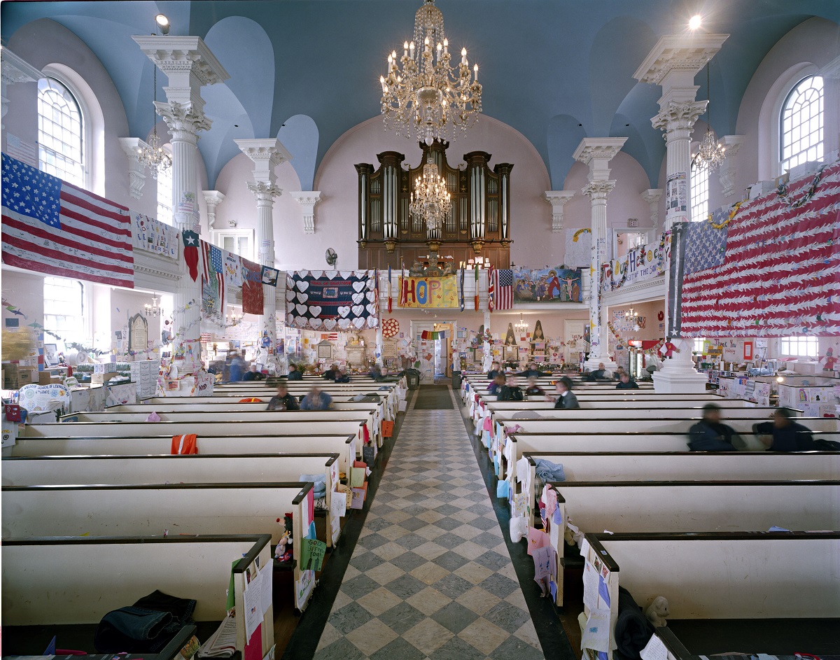 A photo from inside St. Paul’s Chapel in the days after 9/11 shows American flags, tributes, and other items hanging all over the interior of the church. Several people are sitting in the pews.