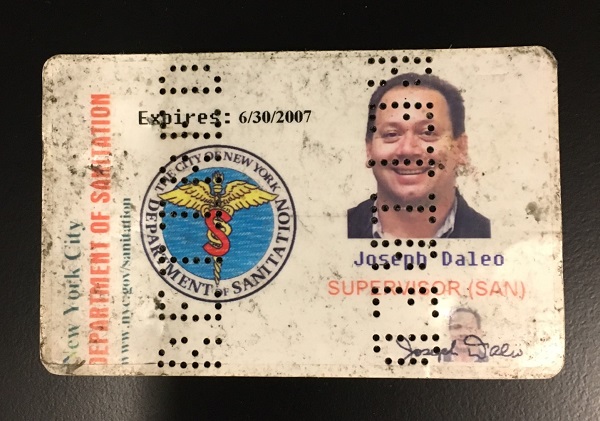 A heavily worn New York City Department of Sanitation identification card issued to Joseph D'Aleo is displayed on a black surface.